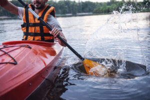 Cropped image of handsome young man in sea vest sailing a kayak