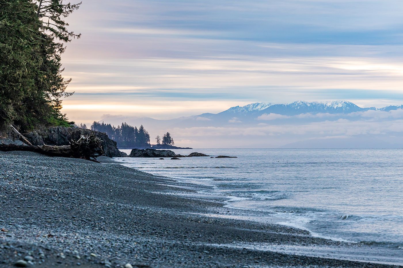 soft, cool sunrise light over a pebbly beach with snowcapped mountains in the distance