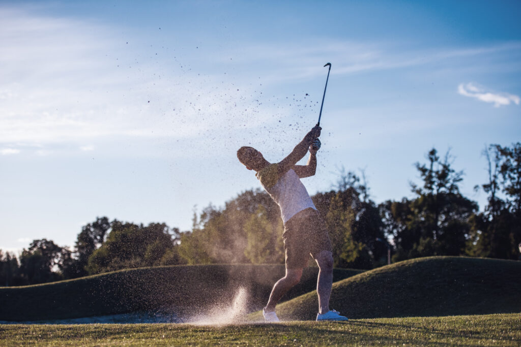 man taking a swing from a sand trap on a golf course - sunny day