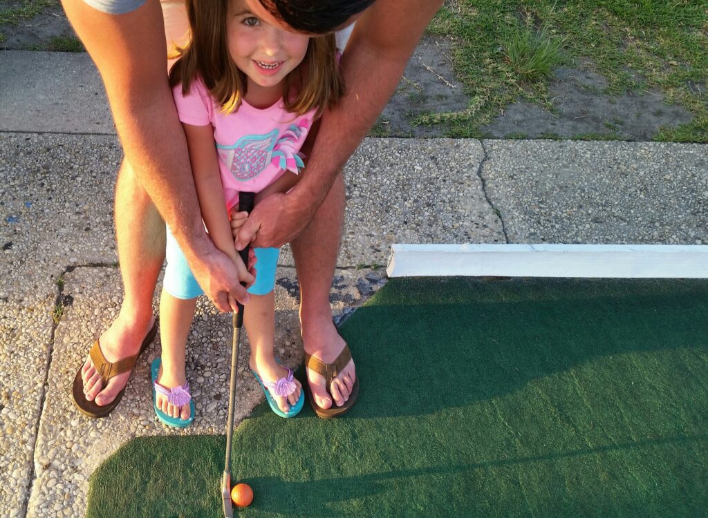 little girl playing mini golf with her parent - family fun