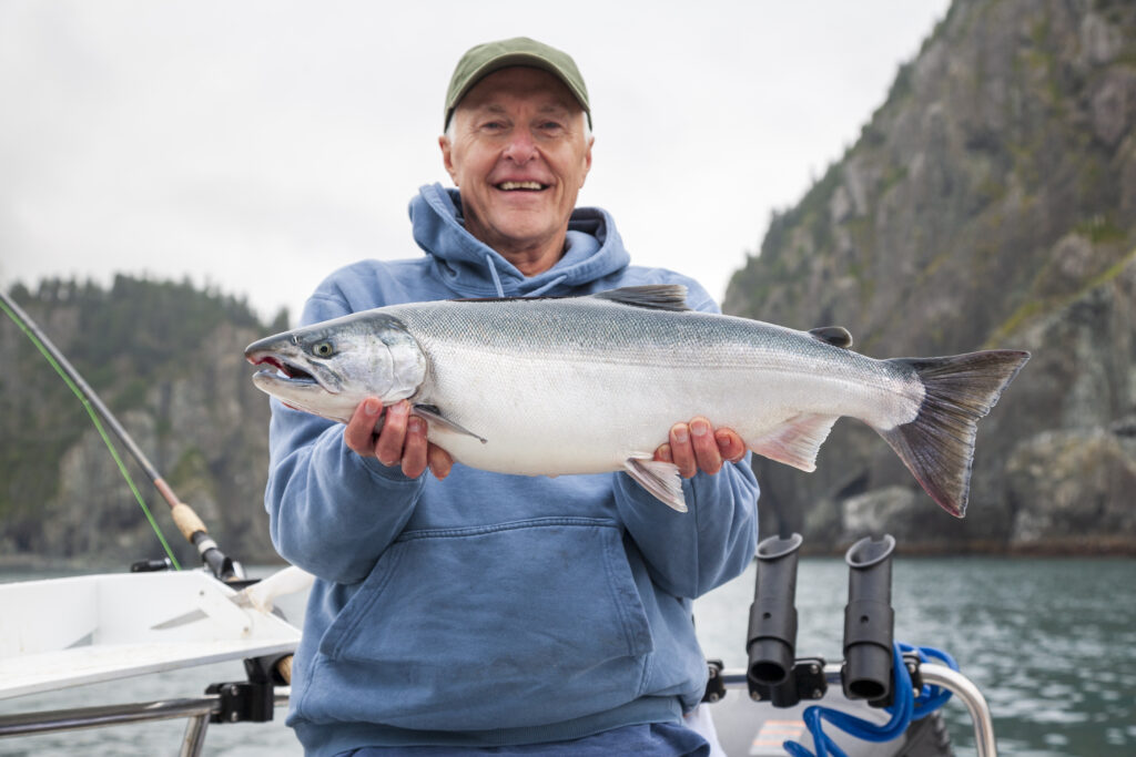 older man wearing a blur hoodie and basball hat holding a large slamon - fishing in bc