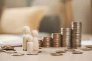 small wooden figures next to pile of coins - cost of living