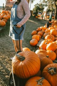 girl in short overalls pulling a wagon with lots of pumpkins inside
