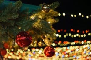 Christmas tree branch decorated with shiny red balls on glowing festive holiday lights background