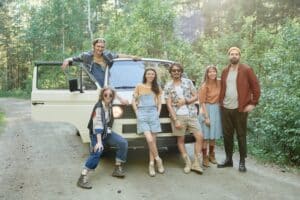 Portrait of group of friends smiling at camera posing near the van they standing in the forest