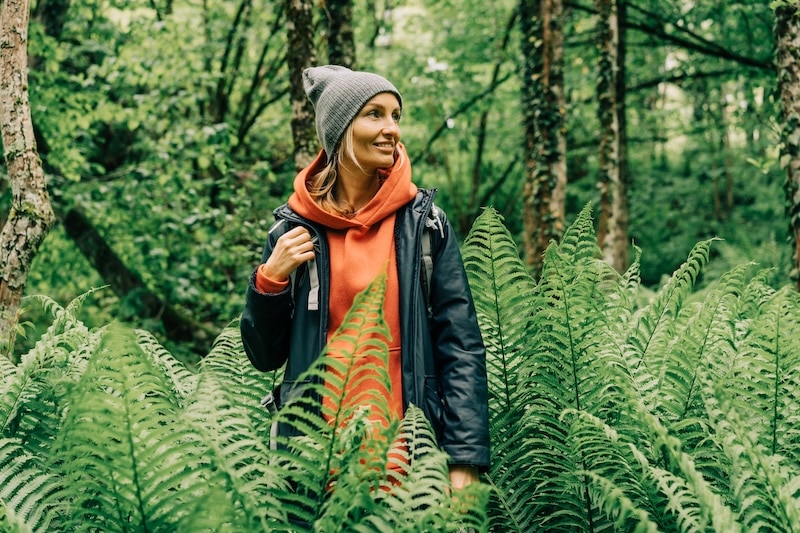Young, blonde woman wearing light layers and a touque in the forest surrounded by ferns - pacific northwest fashion, packing, what to wear